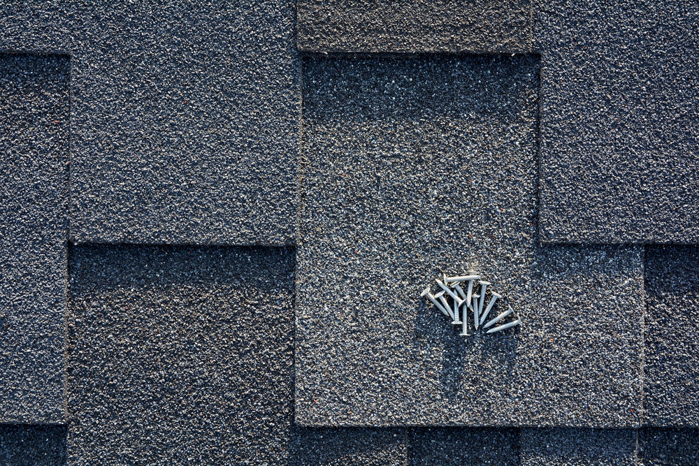 Close,up,view,on,asphalt,roofing,shingles,and,nails,background.